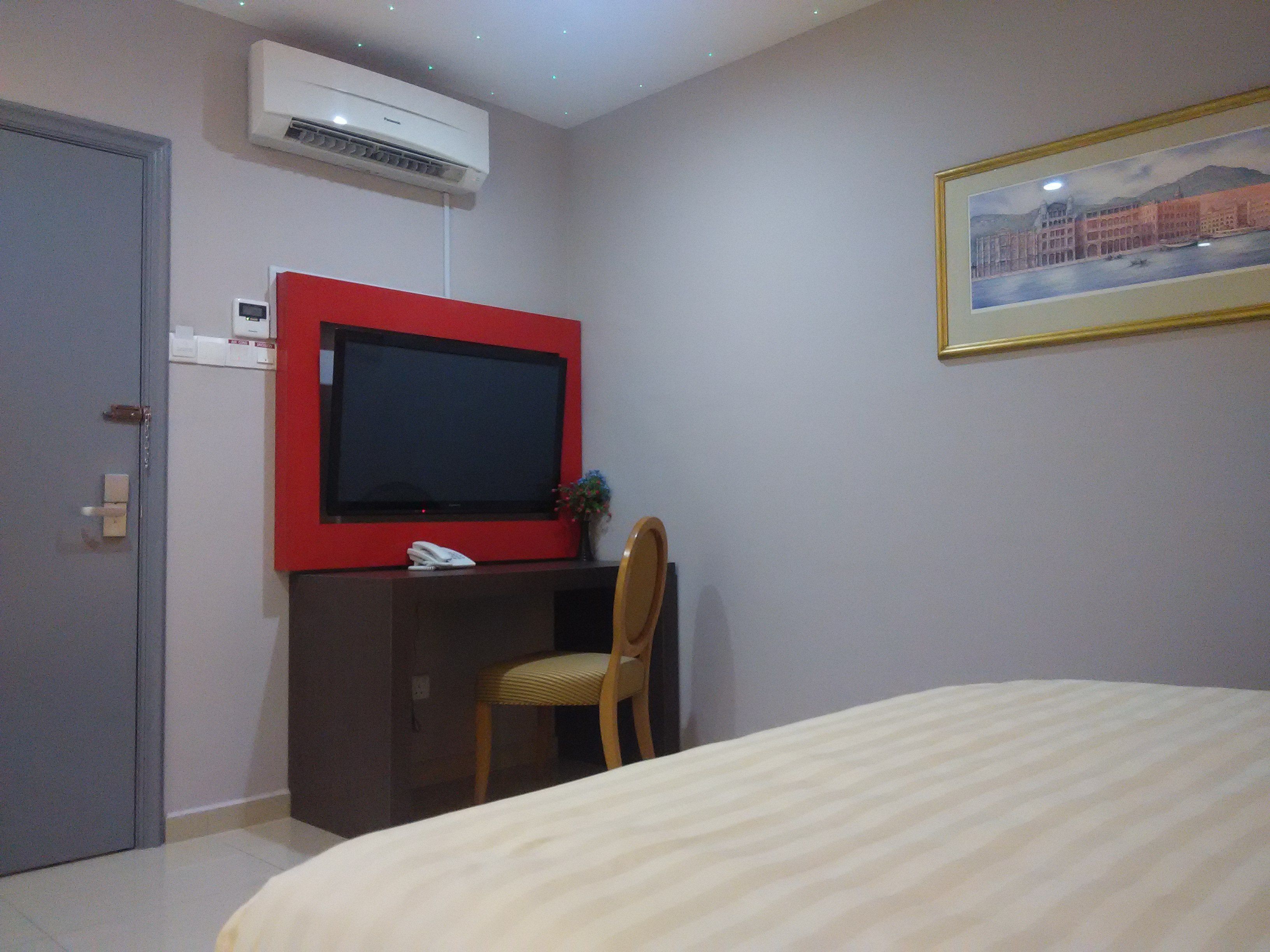 Una habitación de hotel con cama, escritorio con televisor, silla y un cuadro en la pared.