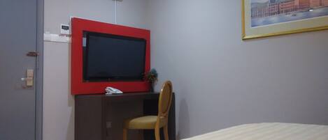 Una habitación de hotel con cama, escritorio con televisor, silla y un cuadro en la pared.