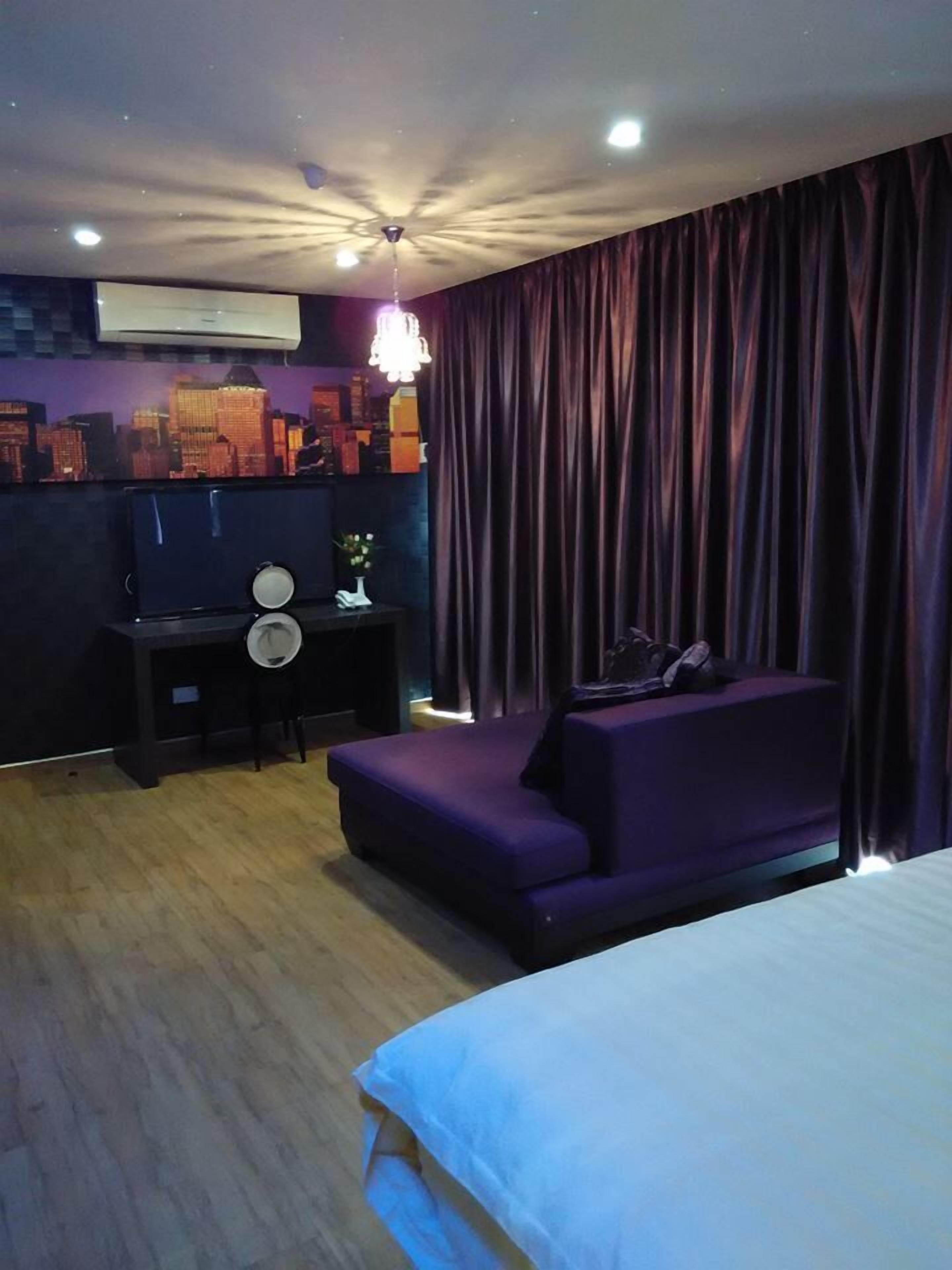 A modern hotel room with a bed, a desk, a chair, and a purple sofa.