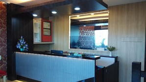 A modern reception desk with a glass partition, a small plant, and a digital screen.