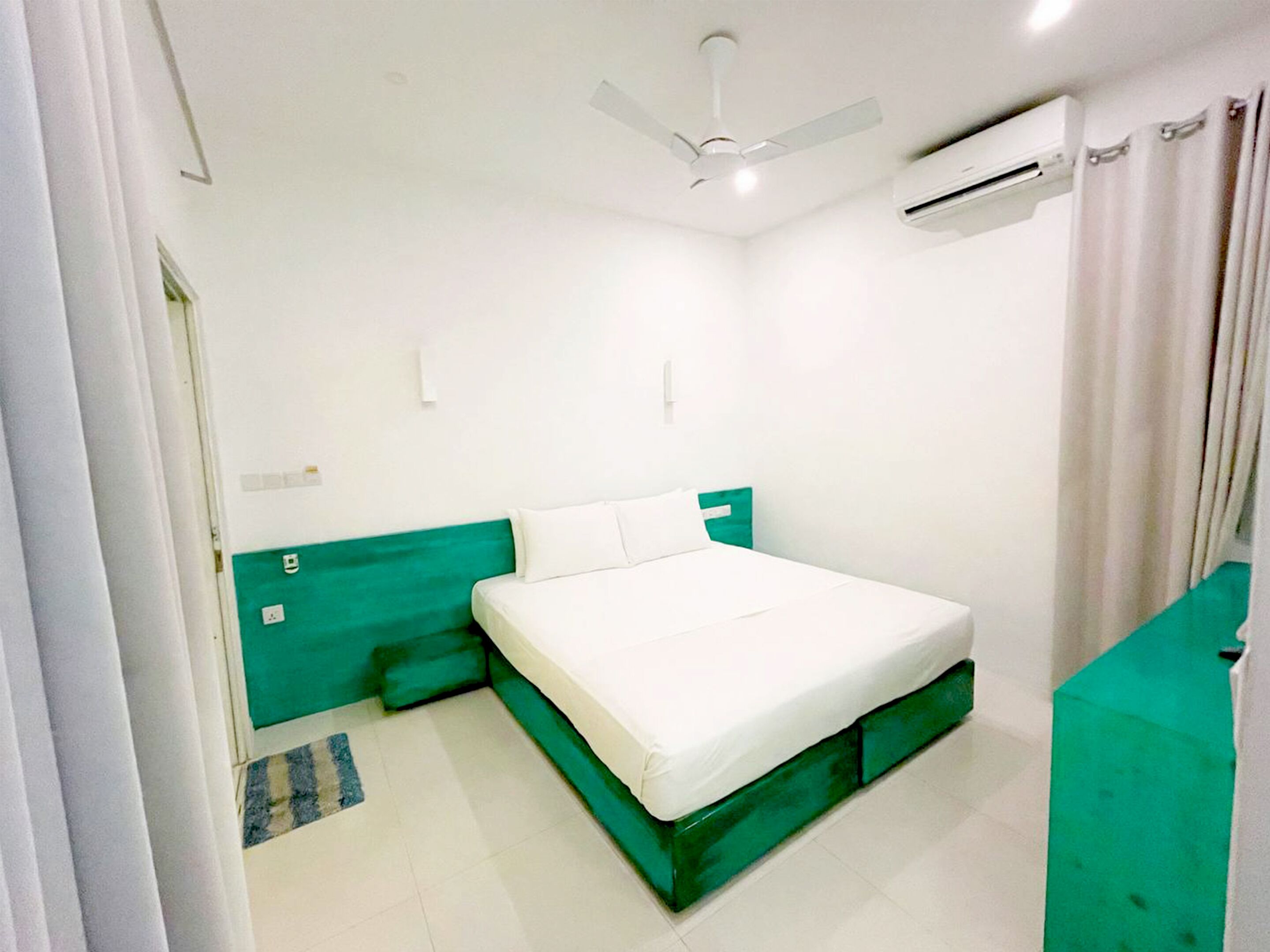 Een slaapkamer met een bed, een plafondventilator, een airconditioning en een groene accentmuur.