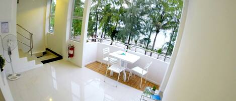 Una habitación moderna y luminosa con balcón, muebles blancos y vistas a árboles y a la playa.