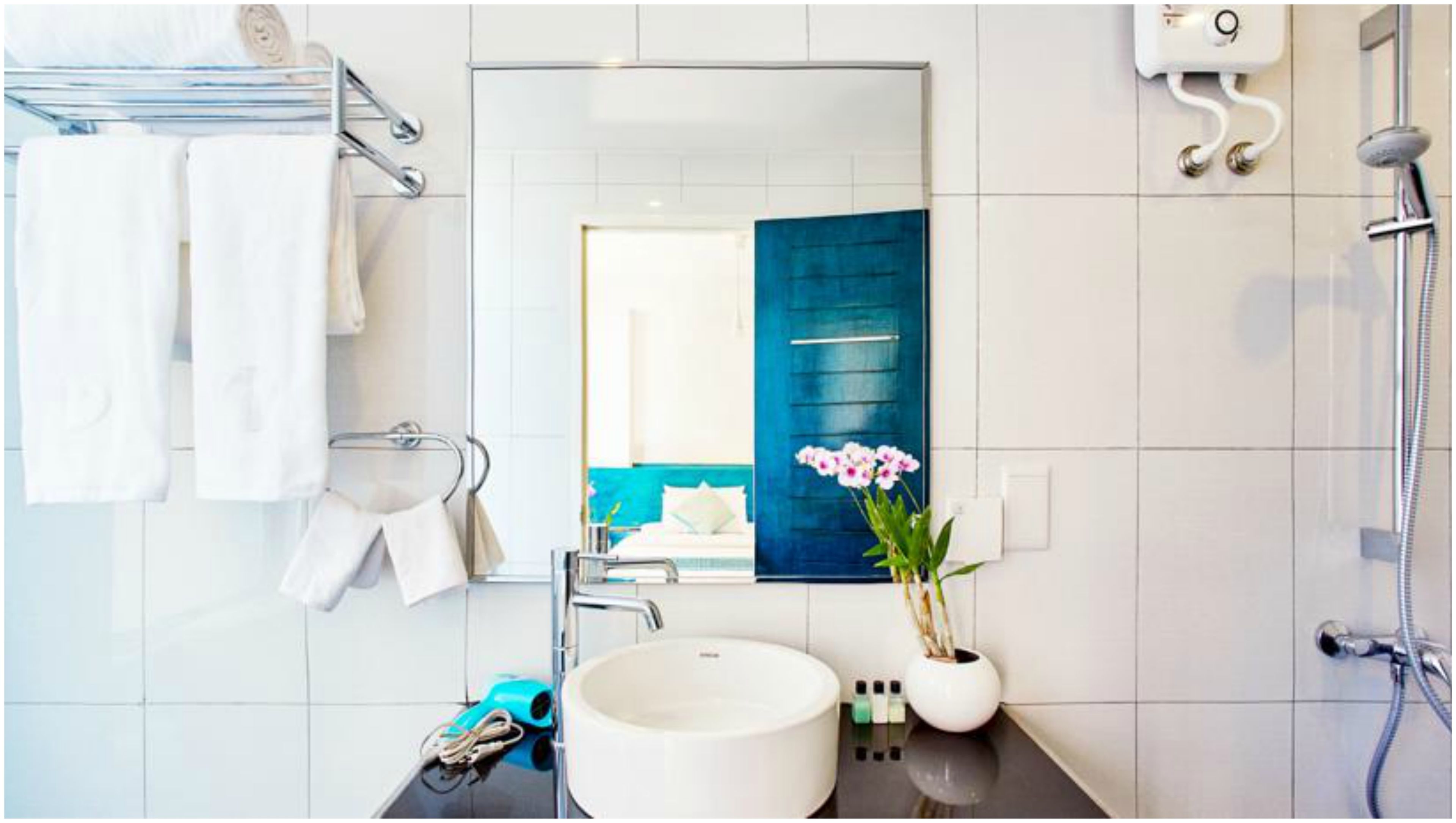 A modern bathroom with a large mirror, white tiles, a round sink, a towel rack, a shower, and a potted plant.