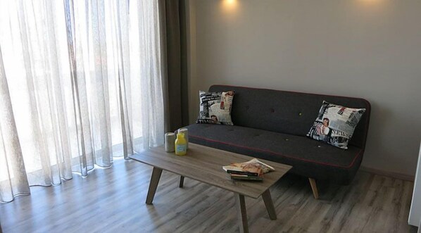 Ein modernes Wohnzimmer mit einem grauen Sofa, zwei gemusterten Kissen, einem Holztisch und einer Wasserflasche.