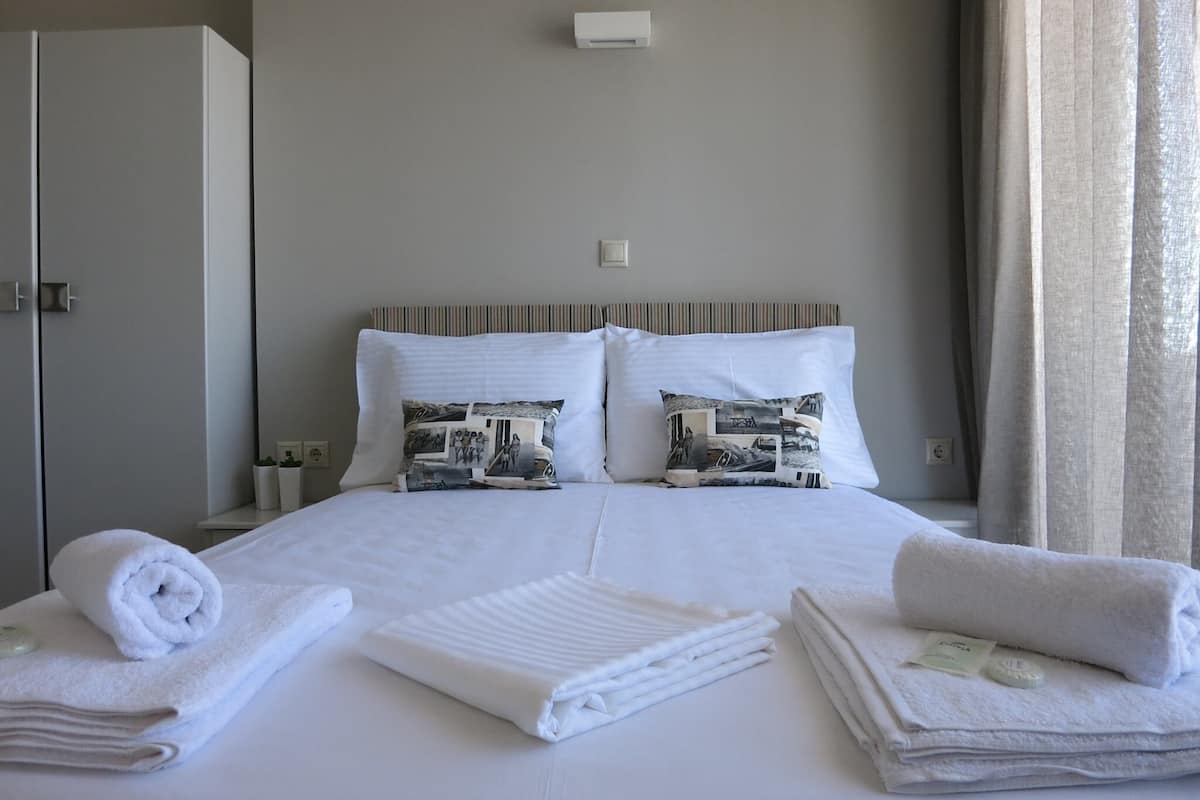 A neatly made bed with two pillows, a bedside table with a lamp, and a window with curtains.
