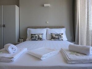 Ein ordentlich bezogenes Bett mit zwei Kissen, ein Nachttisch mit Lampe und ein Fenster mit Vorhängen.