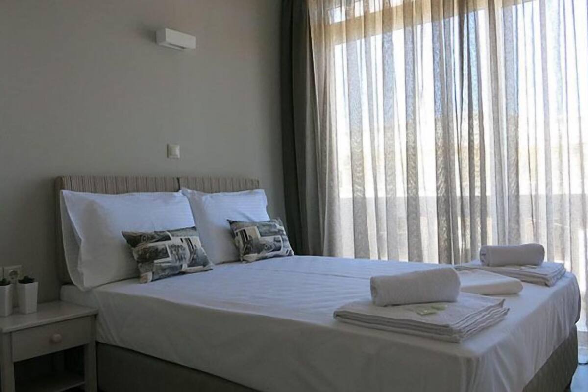 A hotel room with a bed, pillows, a nightstand, and a window with curtains.