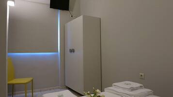 Una habitación con cama, armario, silla y televisor montado en la pared.