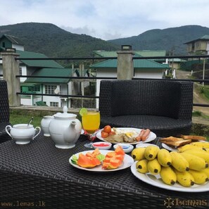 Una colazione allestita con un tavolo, una sedia in vimini e vista su un edificio con tetti verdi.