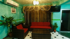 A living room with a red sofa, wicker furniture, a television, and a potted plant. - Off Day Inn Hotel (Malé)