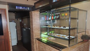 A kitchen area with a glass display case containing food items and beverages. There is a refrigerator and a sink in the background. - Off Day Inn Hotel (Malé)