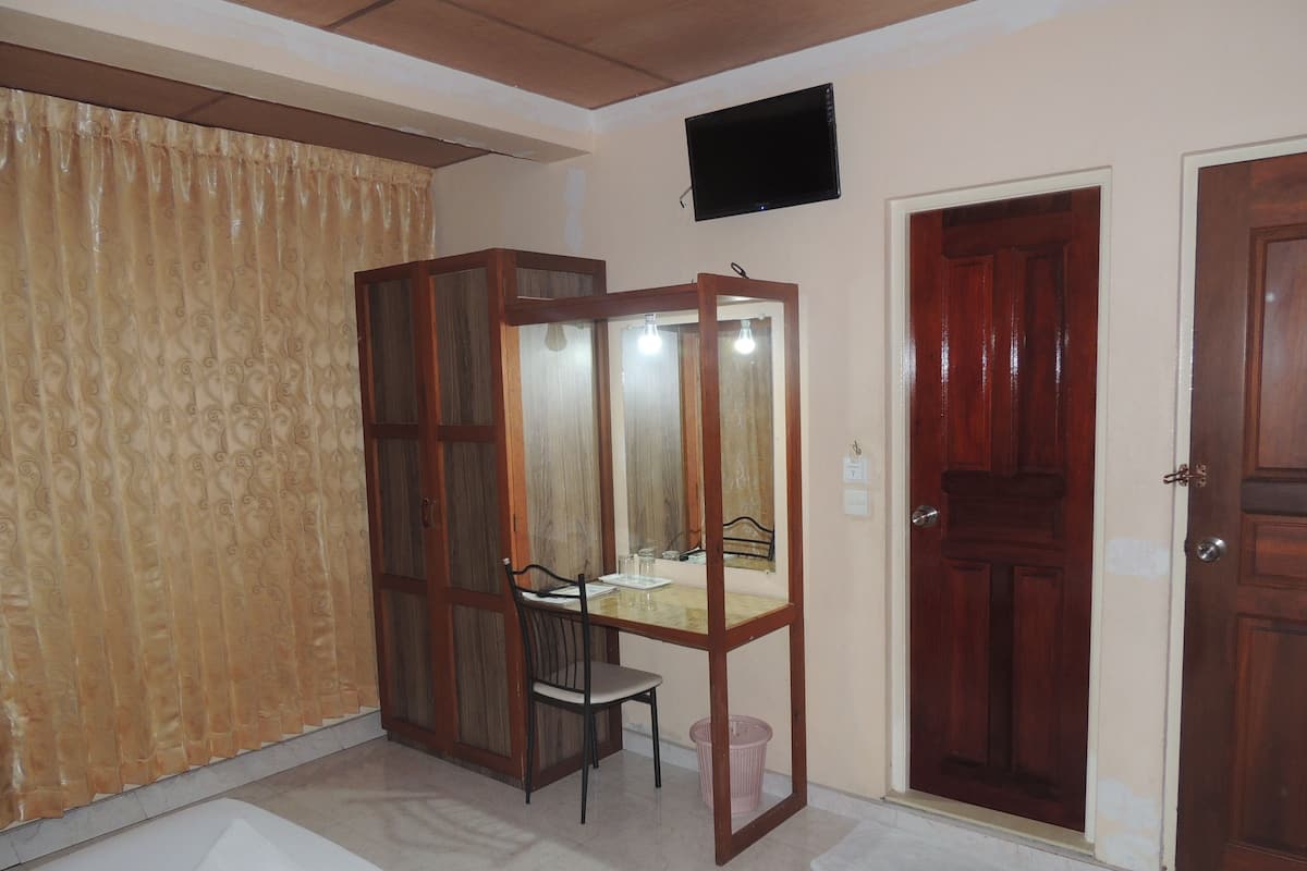 A room with a wooden desk, a chair, a mirror, a television mounted on the wall, and two wooden doors.