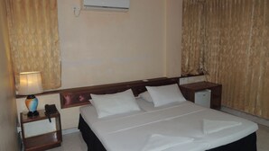 A hotel room with a bed, a nightstand, a lamp, and an air conditioning unit on the wall. - Off Day Inn Hotel (Malé)