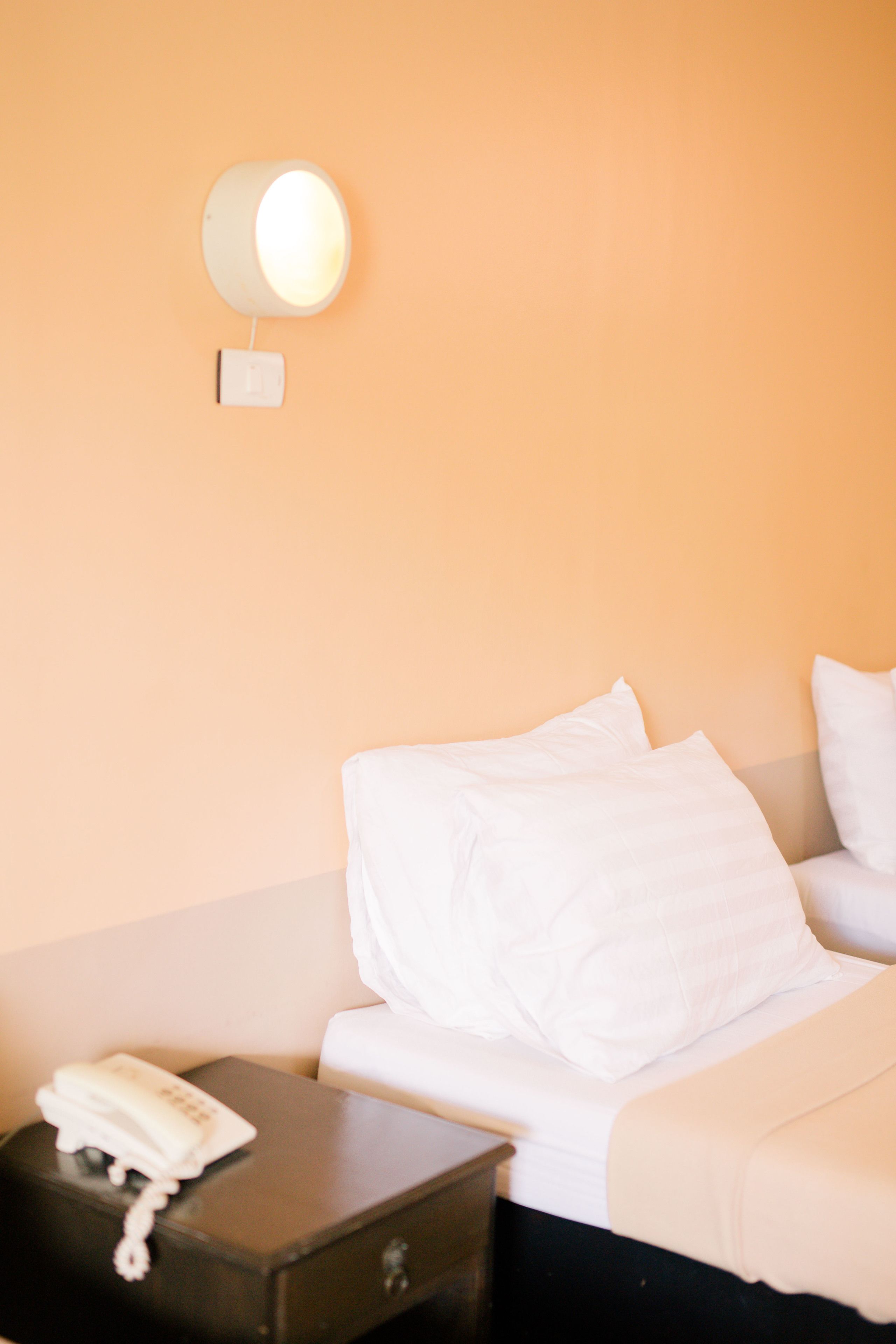 Een hotelkamer met een bed, een nachtkastje met een telefoon en een wandlamp.