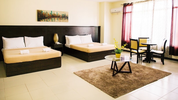A hotel room with two beds, a small table with a vase, and a painting on the wall. - Ati-Atihan Festival Hotel (Kalibo)