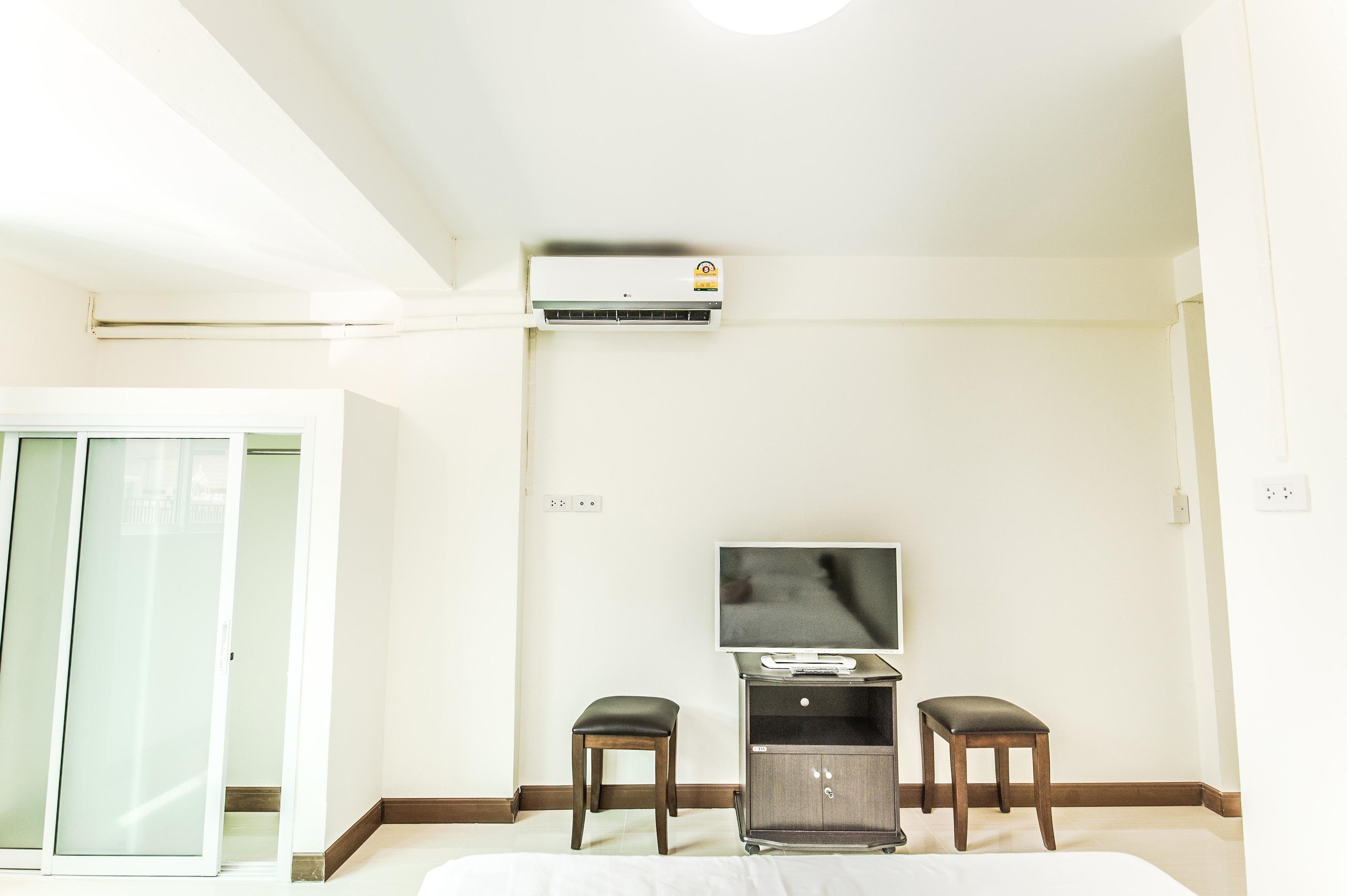 A hotel room with a bed, a television on a stand, a small table, two chairs, an air conditioning unit, and a sliding glass door.