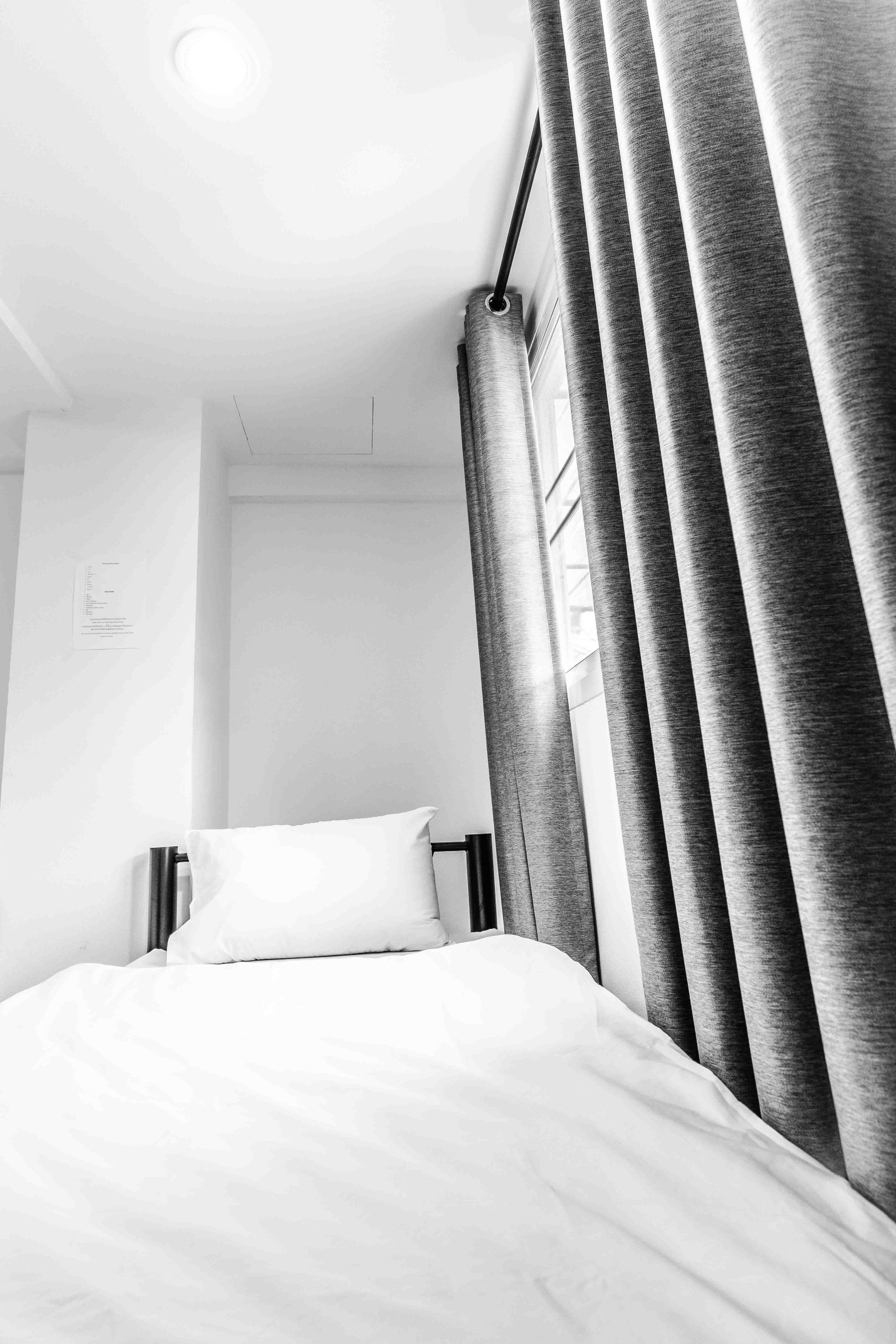 A modern hotel room with a neatly made bed, a nightstand, and a window with curtains.