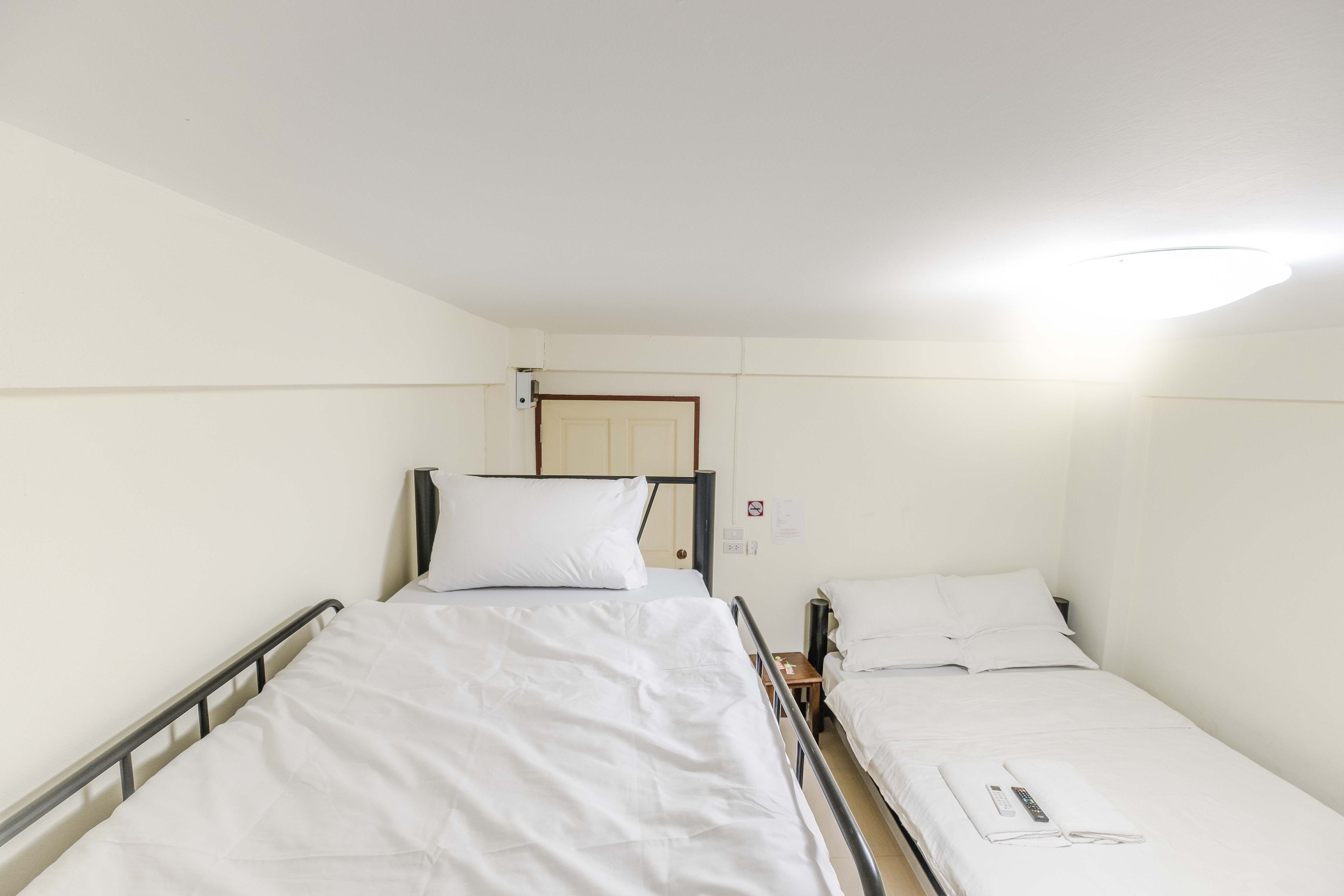 A single-bed room with a wooden door, a bedside table, and a bed with white bedding.