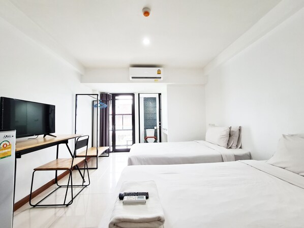 A hotel room with a flat-screen TV, a desk, two beds, and a view of the outside. - Don Muang Hotel (Bangkok)