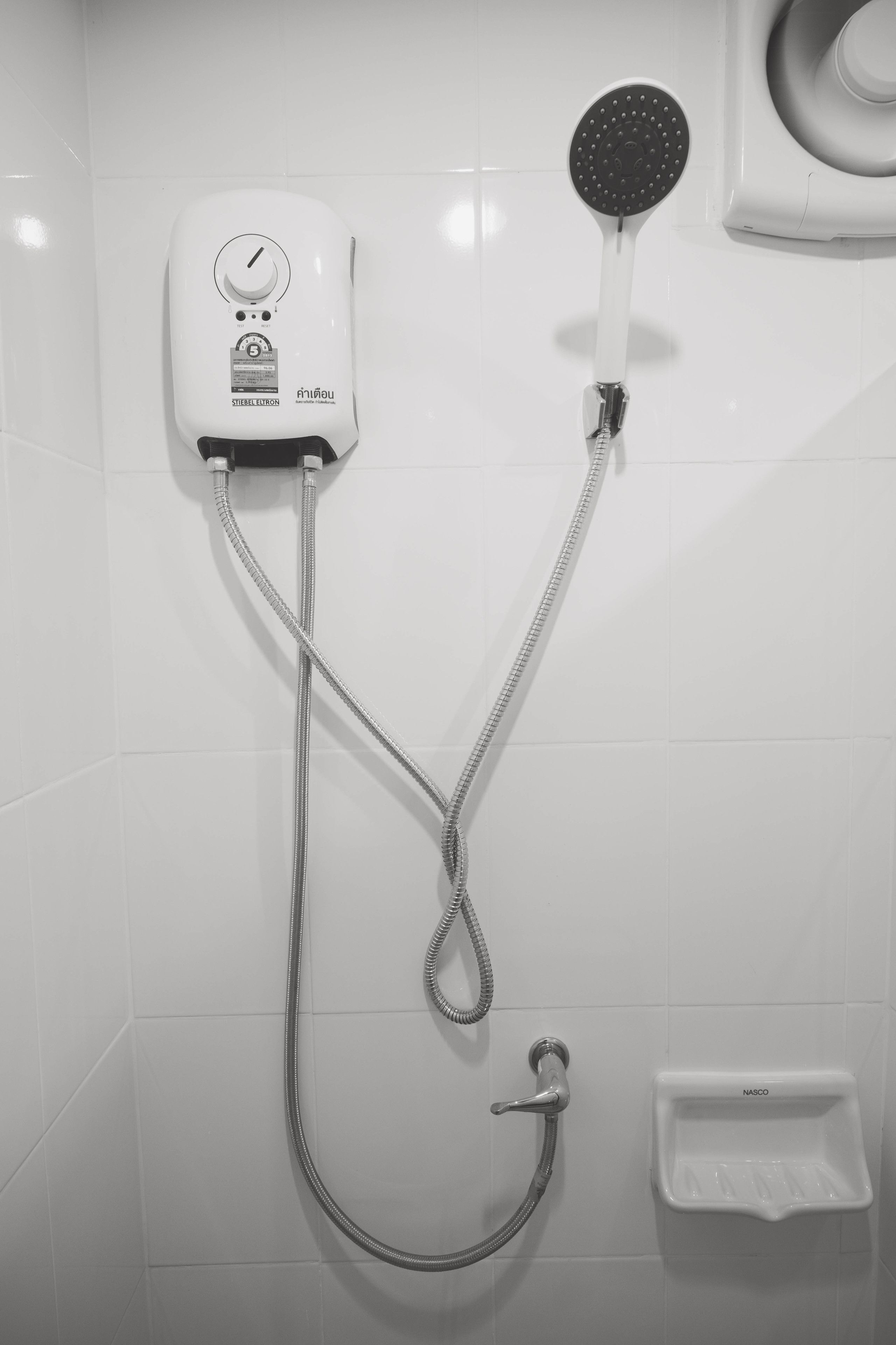 A wall-mounted shower unit with a handheld showerhead and a control panel.