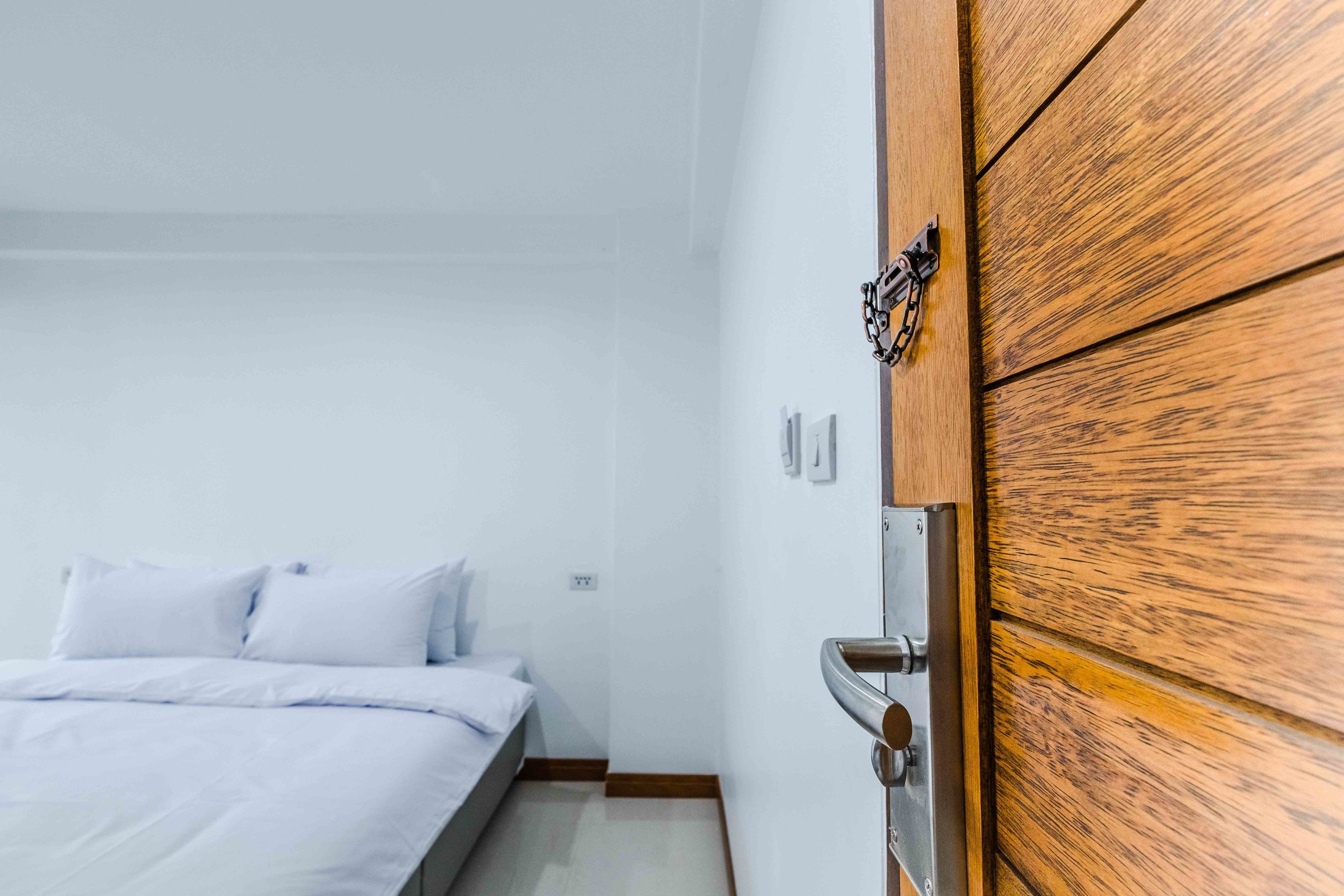 A bedroom with a wooden door, a bed with white bedding, and a small bedside table.
