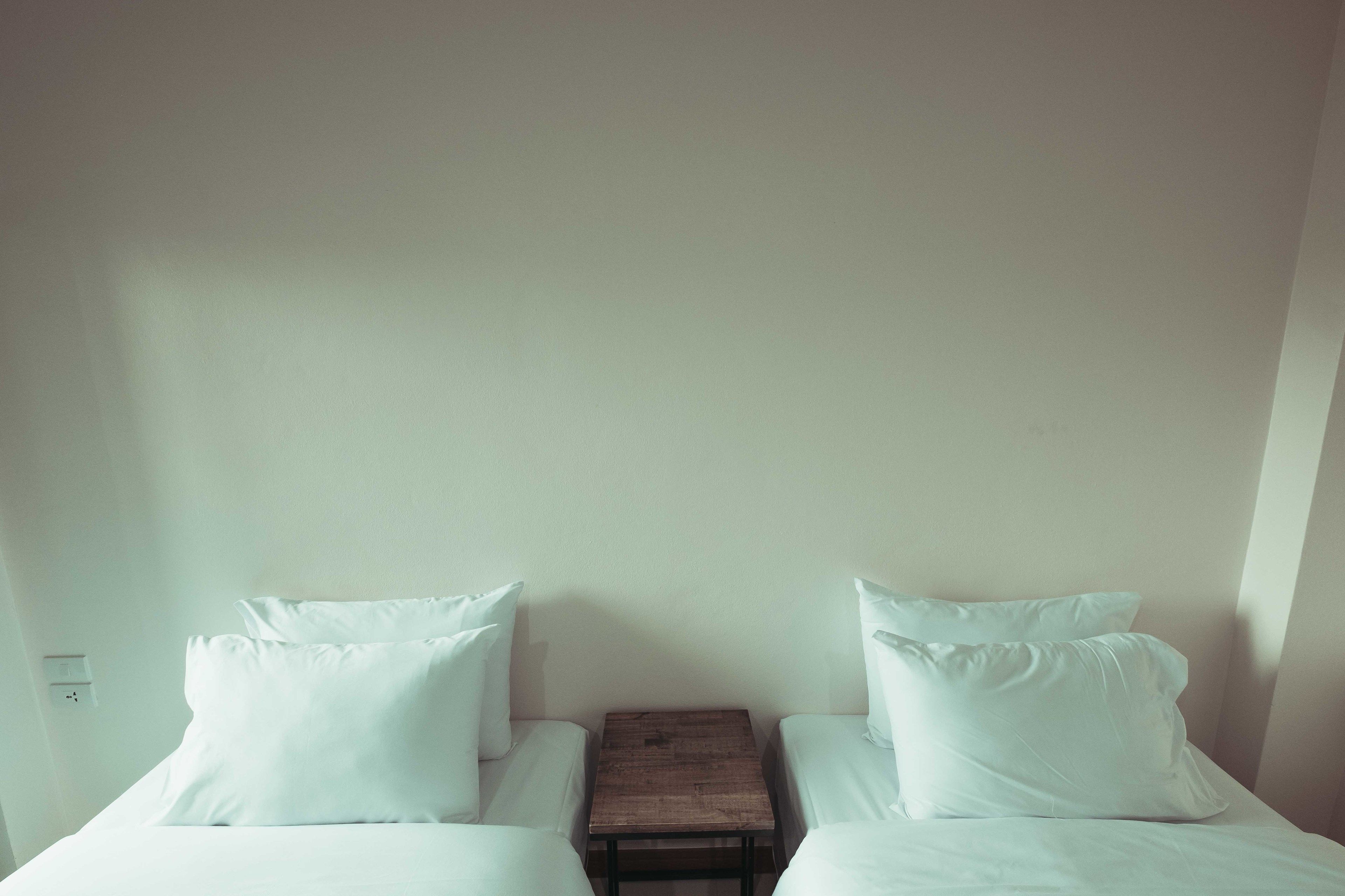 A simple room with two beds, a small wooden nightstand, and a white wall.