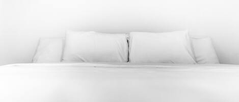 A bed with white bedding and pillows against a plain wall.