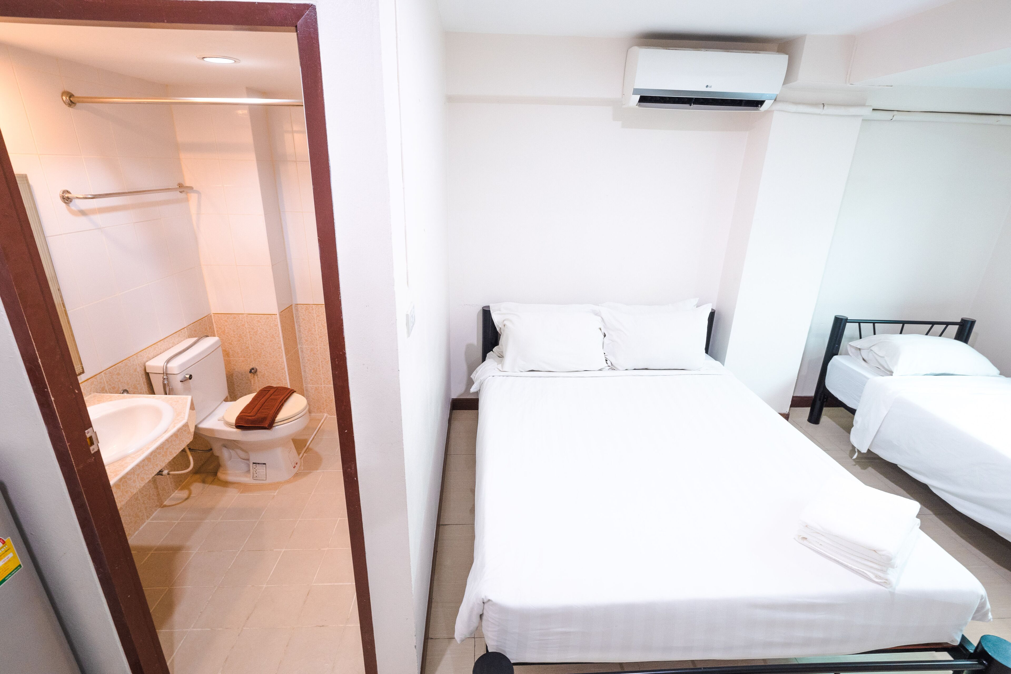 Habitación de hotel con una cama grande, una mesita de noche pequeña, un baño independiente con inodoro y lavamanos, y una ventana.