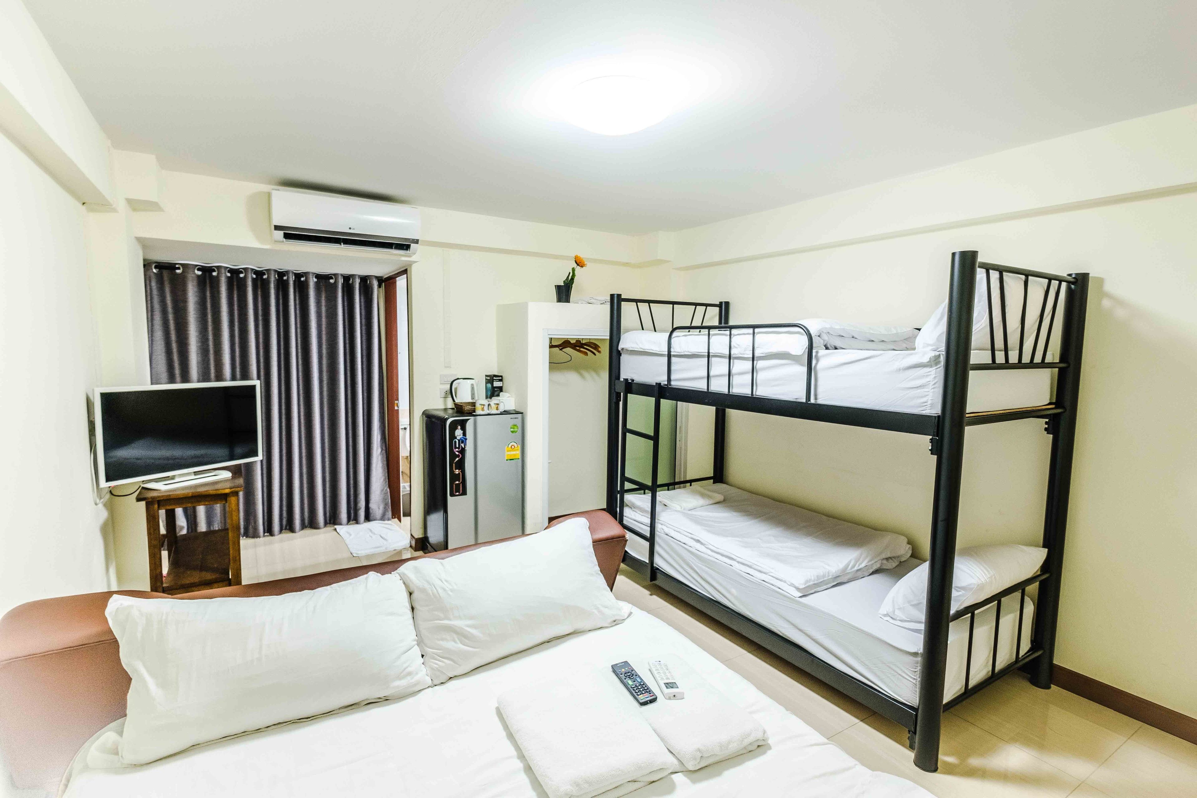 Habitación de hotel con literas, una cama individual, un televisor, un escritorio con ordenador y un armario.