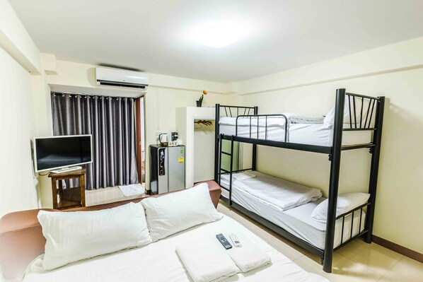 A hotel room with a bunk bed, a single bed, a TV, a desk with a computer, and a wardrobe. - Don Muang Hotel (Bangkok)