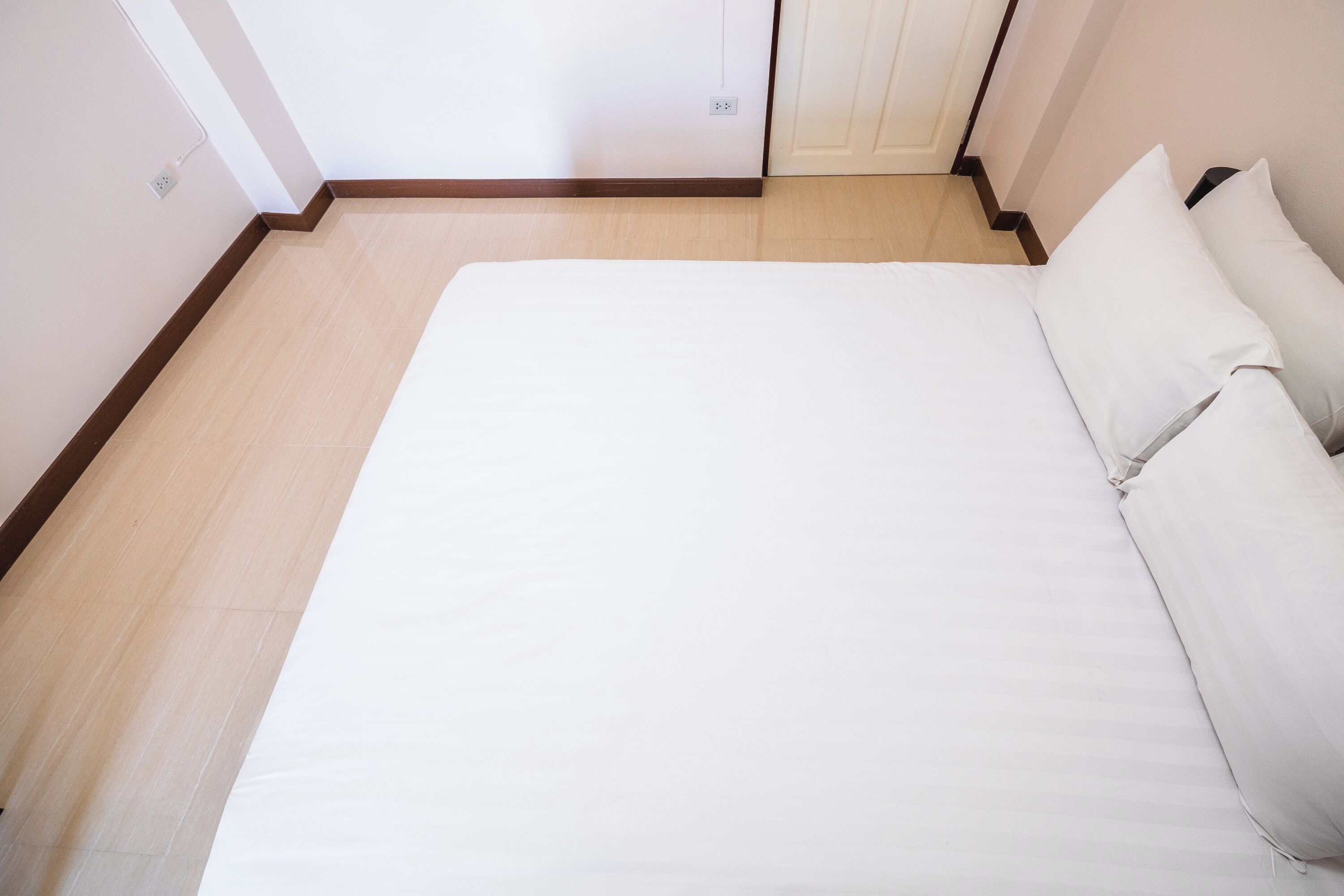 A bedroom with a bed, a wooden floor, and a white wall.