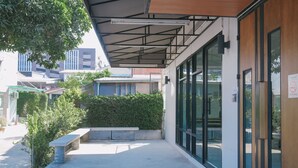 An outdoor area with a bench, a covered walkway, and a building with large windows. - Don Muang Hotel (Bangkok)