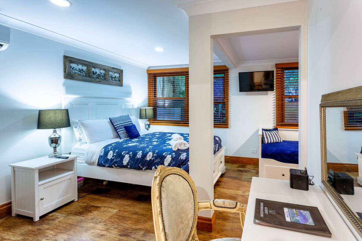 A bedroom with a bed, bedside tables, a desk, a chair, a mirror, and a TV.