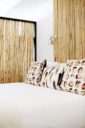 A bed with patterned pillows, a bamboo wall, and a white ceiling.