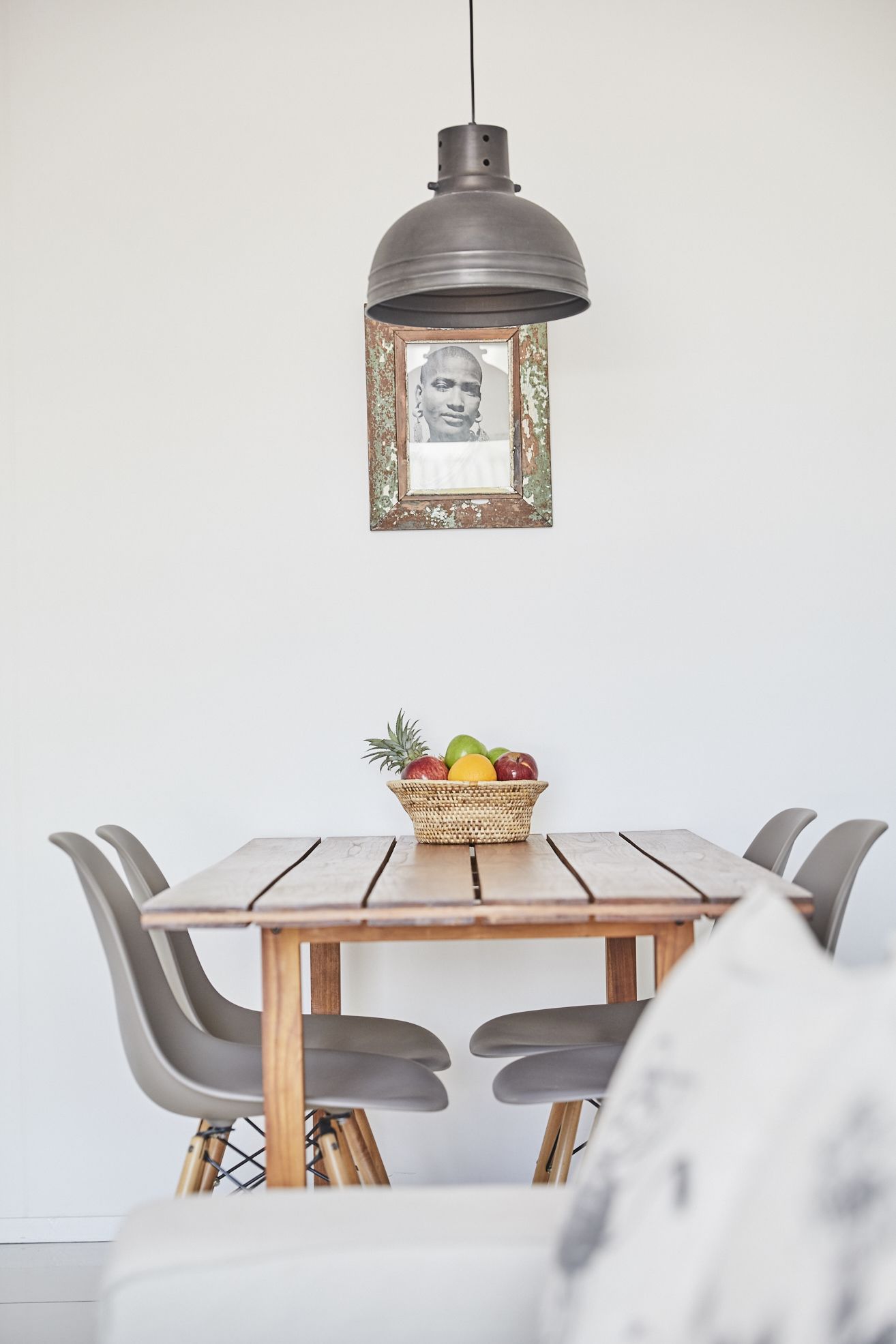 A dining area with a wooden table, a woven basket of fruit, and a pendant light.