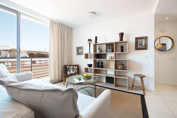 A modern living room with a sofa, a glass coffee table, and a bookshelf.