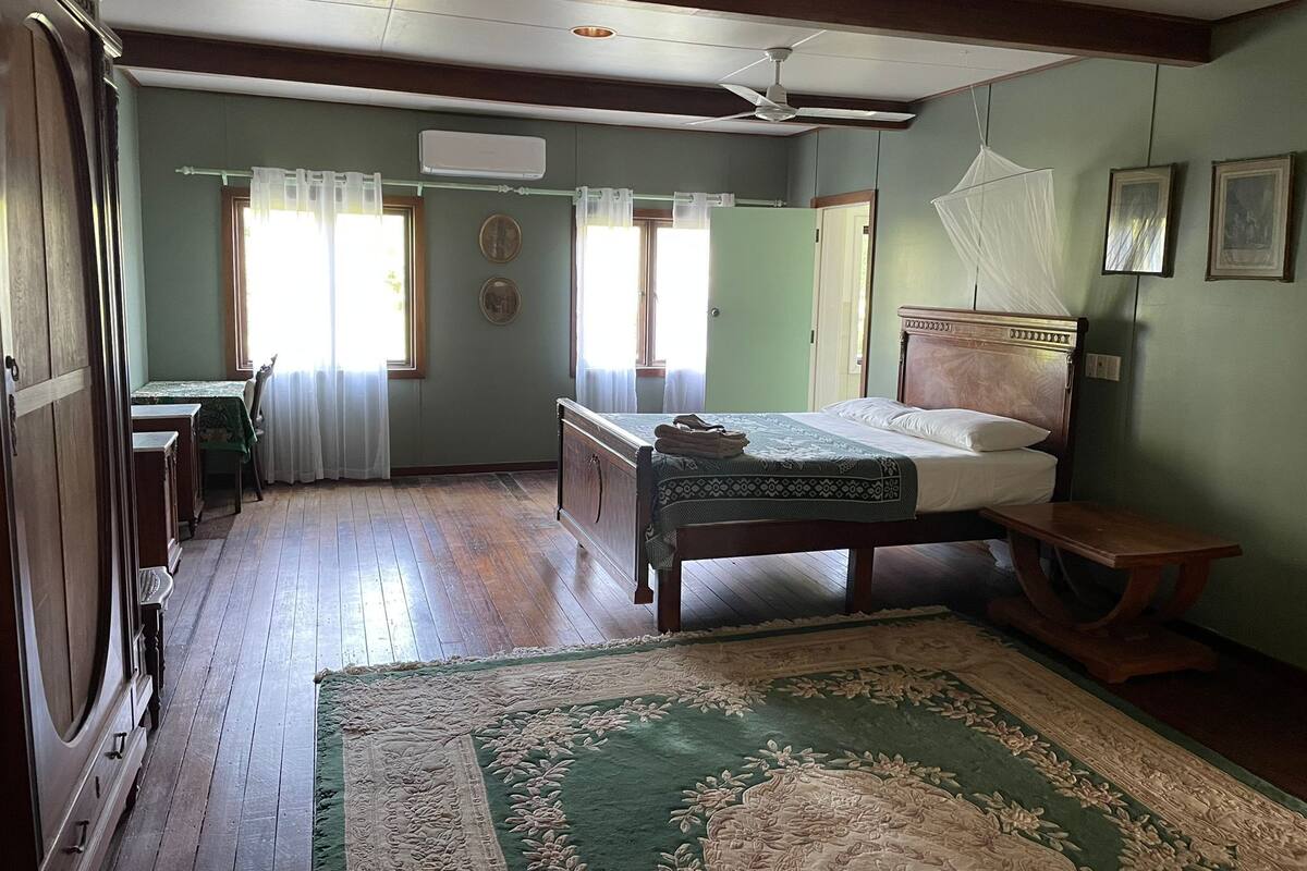 A room with a wooden bed, a desk, a chair, and a large green patterned rug.