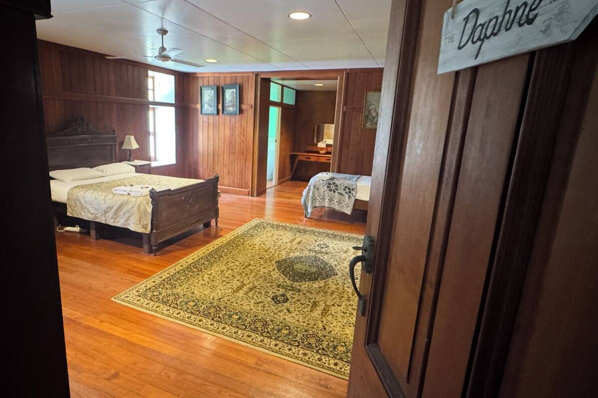 A room with wooden walls, a bed with a white bedspread, a nightstand, a lamp, and a sign reading "Dahabe ROOM".