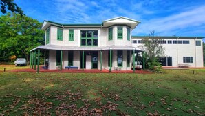 A two-story building with a covered porch, a carport, and a lawn with scattered leaves. - Oceania House (Home Island)
