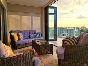Un balcon aménagé avec un canapé, des fauteuils en osier et une porte vitrée donnant sur une terrasse.