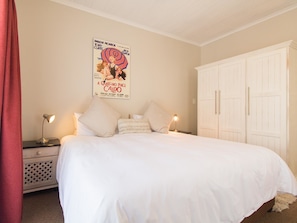 Een slaapkamer met een groot bed, twee nachtkastjes met lampen, een kledingkast en een poster aan de muur.