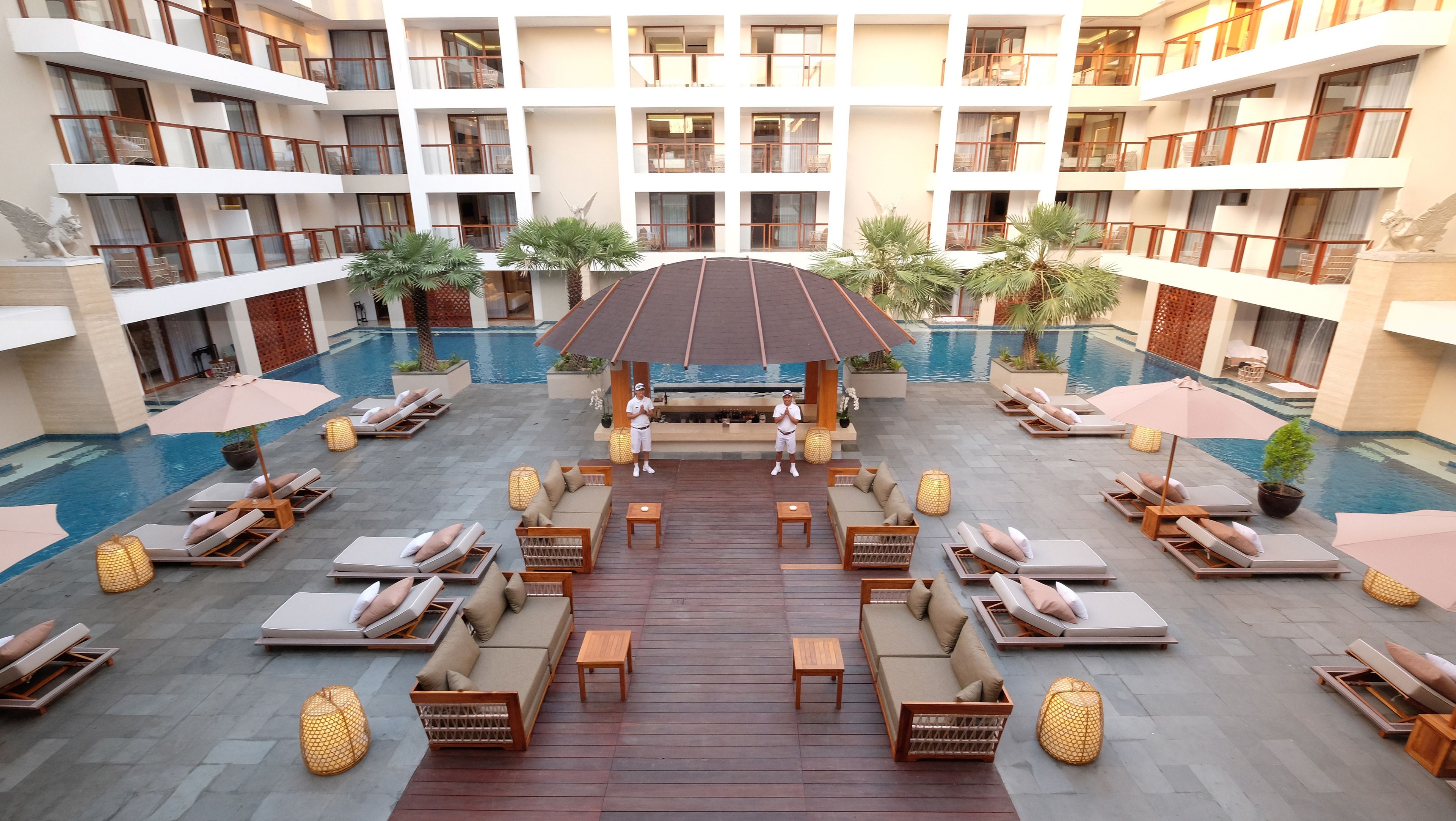 A multi-level hotel with a central pool area featuring sun loungers, seating, and a wooden deck.