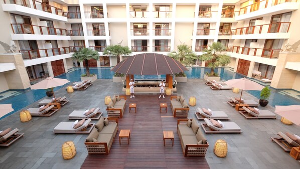 A multi-level hotel with a central pool area featuring sun loungers, seating, and a wooden deck.