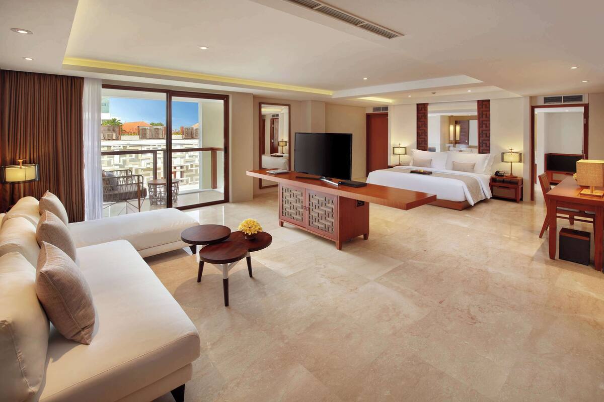 Habitación de hotel con una cama grande, televisión, sofá, escritorio y balcón con vistas.