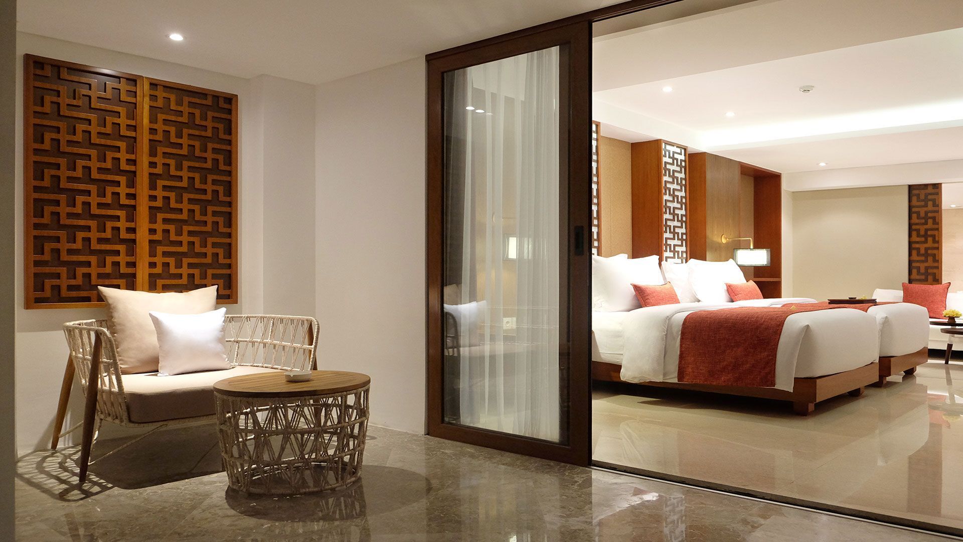 A hotel room with a large bed, a seating area with a chair and a round table, and a decorative wooden panel on the wall.