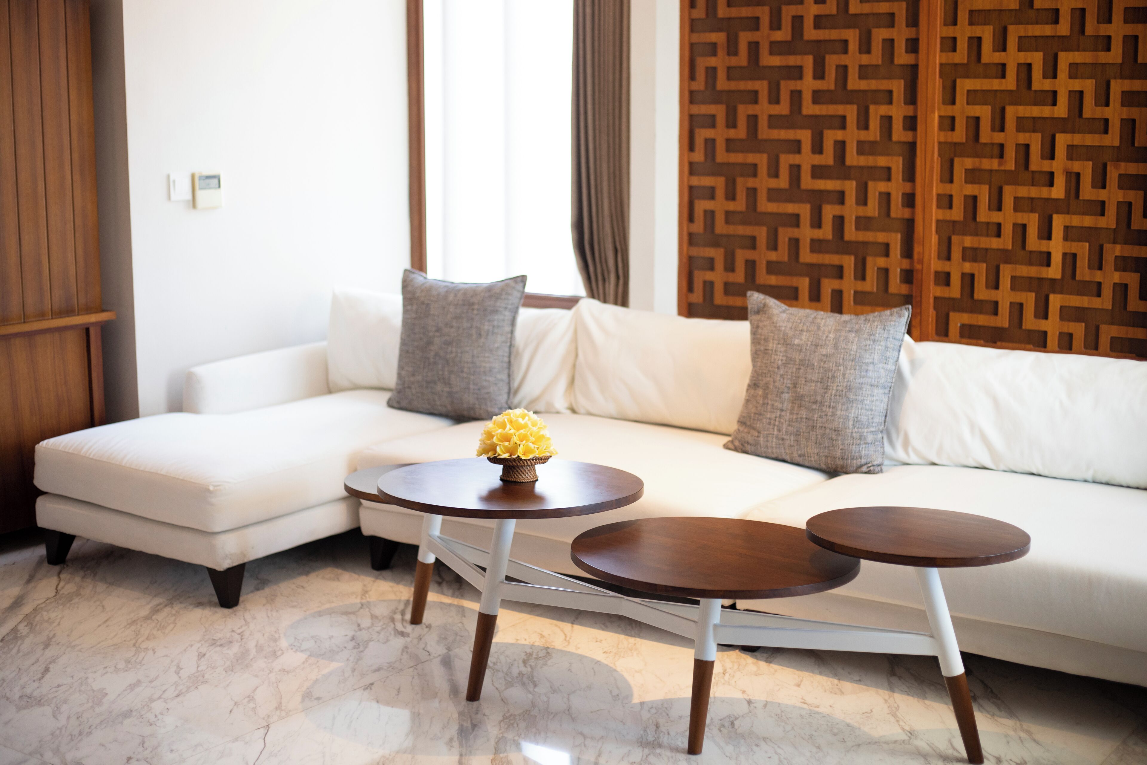 A modern living room with a white sofa, two round wooden side tables, and a decorative vase.