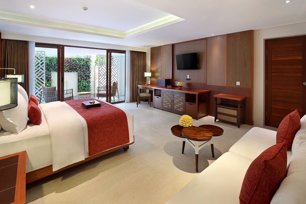 Habitación de hotel con cama, sofá, escritorio con computadora y televisor en la pared.