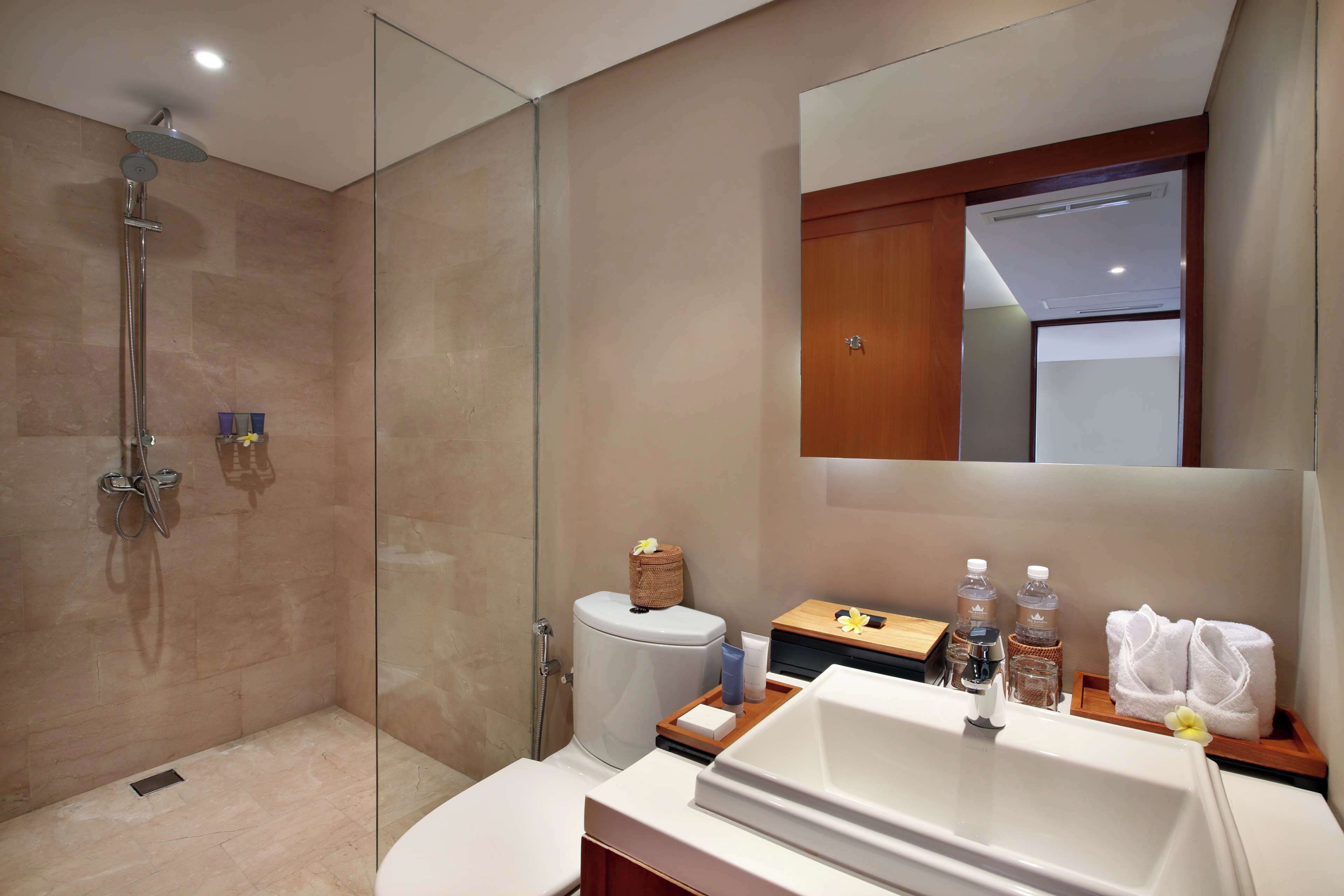 Un baño moderno con ducha de vidrio, inodoro, lavamanos con espejo y tocador de madera.