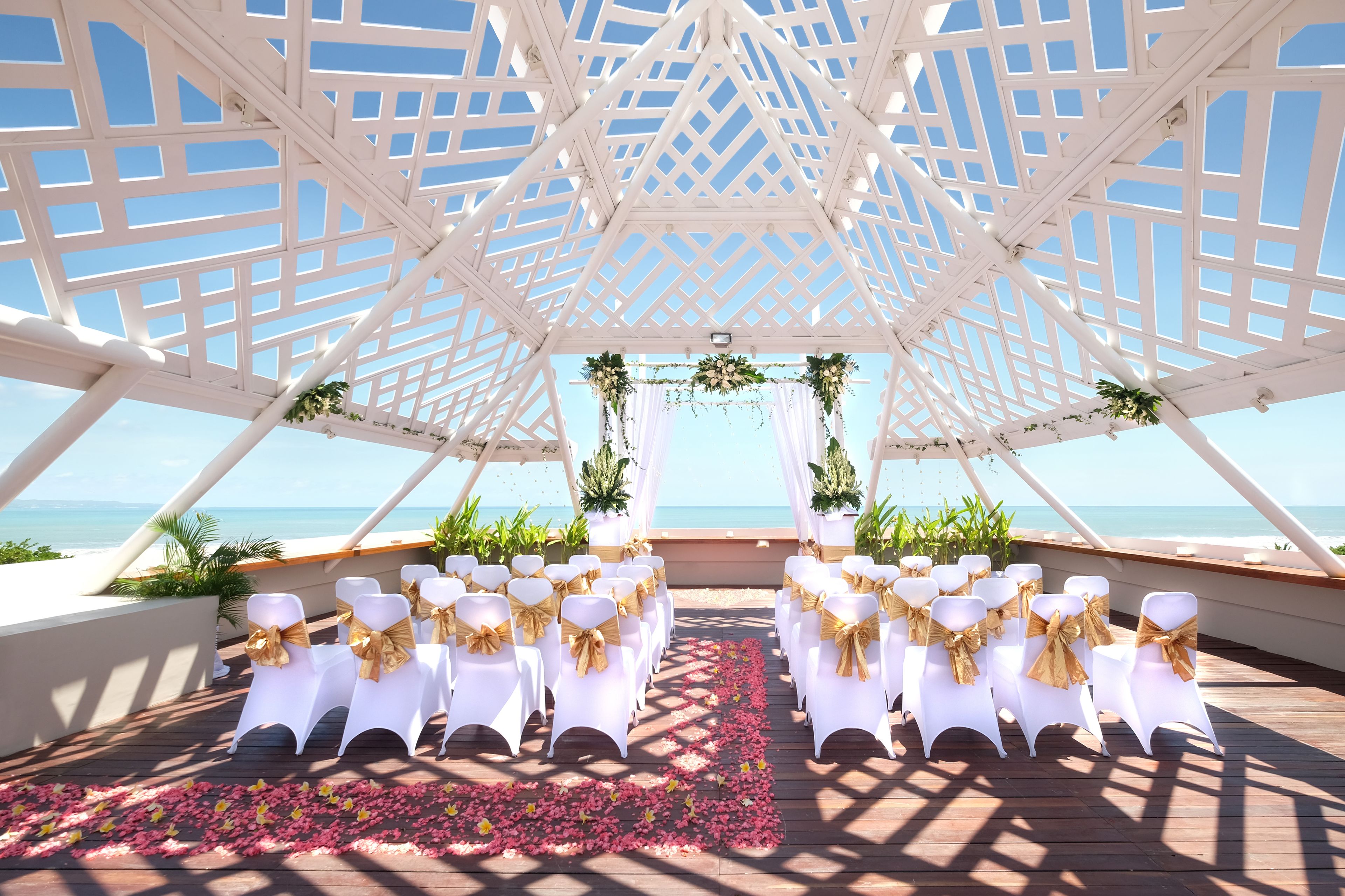 A white gazebo with a wooden floor, arranged seating, and a view of the ocean.