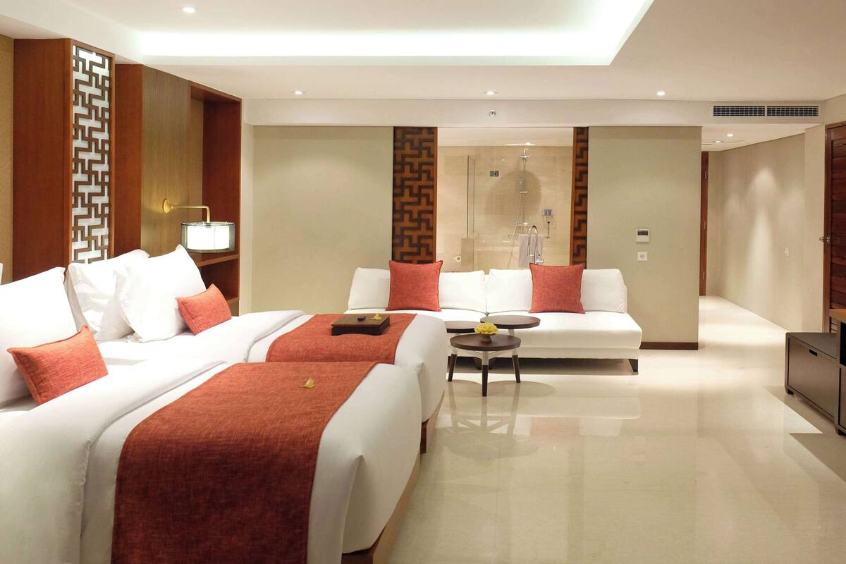 Habitación de hotel con dos camas, un sofá, una mesita y un mini bar.